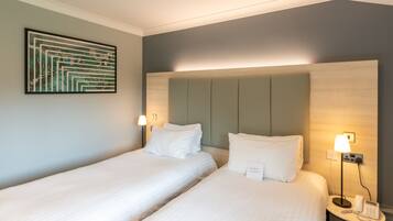 Een hotelkamer met twee bedden, een hoofdbord, bedlampjes, een telefoon en een lijst met kunst aan de muur.