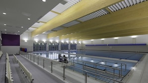 Una piscina interior con techo de madera, paredes con azulejos y un área de estar con bancos.