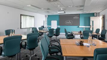 A conference room with teal chairs, a wooden table, and a projector screen displaying "Warwick Conferences".
