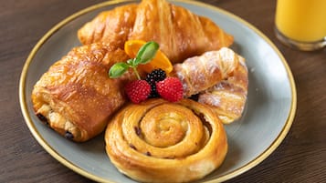 A plate with croissants, a cinnamon roll, fresh berries, and a glass of orange juice on a wooden table.
