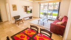 Una sala moderna con un sofá rojo, una mesa de comedor con sillas, un televisor montado en la pared y un gran ventanal corredero que da a un espacio exterior.