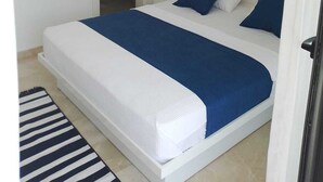 Un dormitorio con cama, baño a la vista a través de una puerta abierta y un cuadro en la pared.