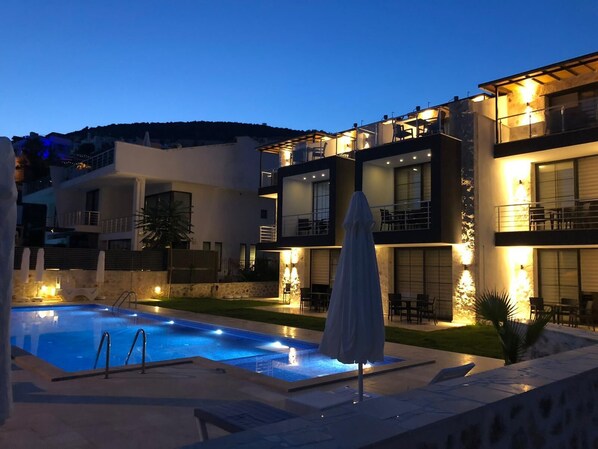 A modern multi-story building with a swimming pool, outdoor seating, and a covered patio area.
