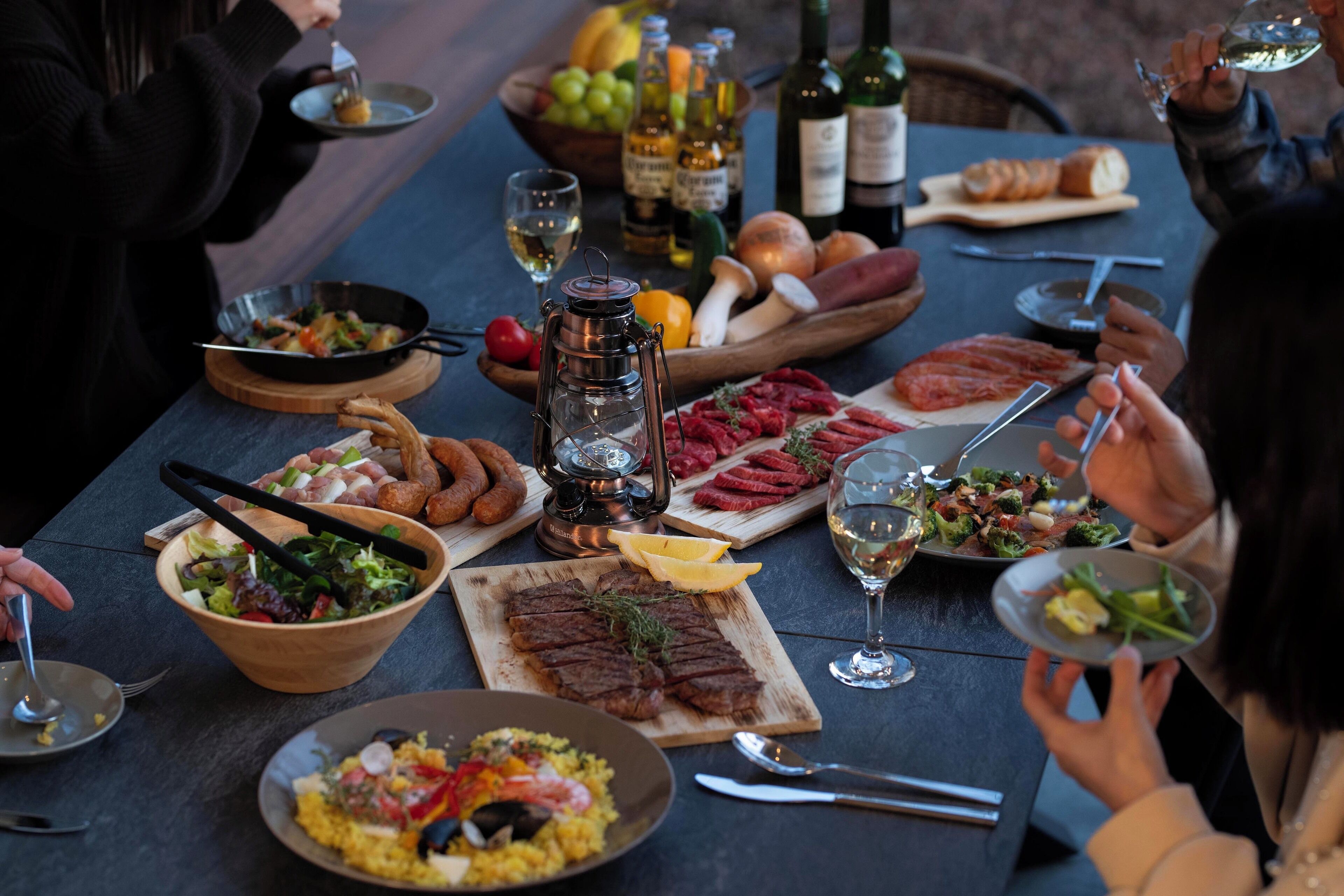 Et spisebord dækket med forskellige retter, heriblandt en salat, bøf og brød, samt vinglas og vinflasker.