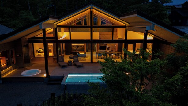 A modern house with a large glass facade, a swimming pool, and a patio area.