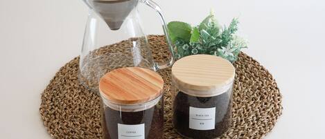 Two glass jars with wooden lids, one labeled "COFFEE" and the other "BLACK TEA," placed on a woven mat.