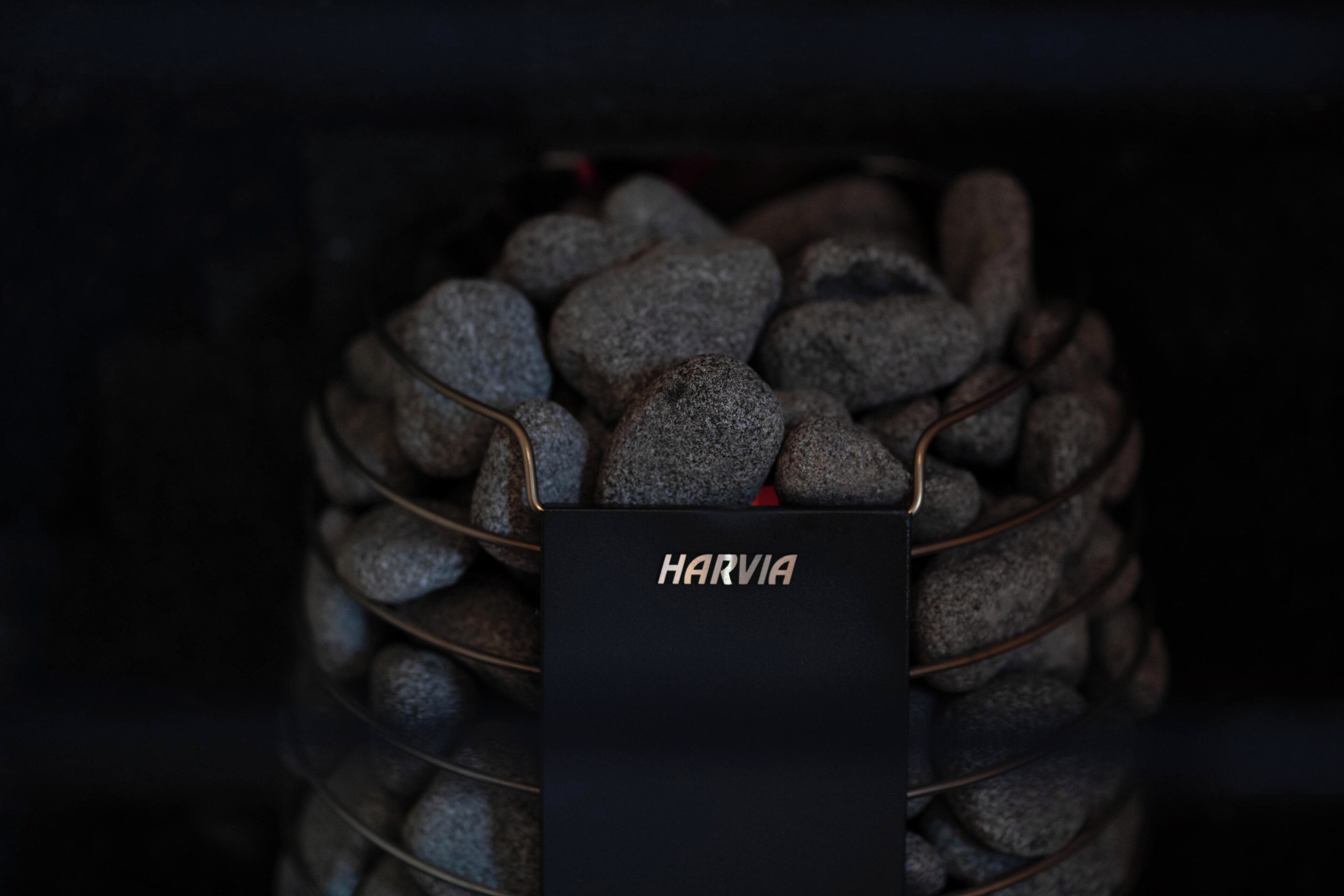 Een zwarte doos met de aanduiding 'HARVIA', voorzien van een metalen draagstructuur en gevuld met talloze grijze stenen.