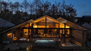 A modern house with a large glass facade, a swimming pool, and a well-lit interior.