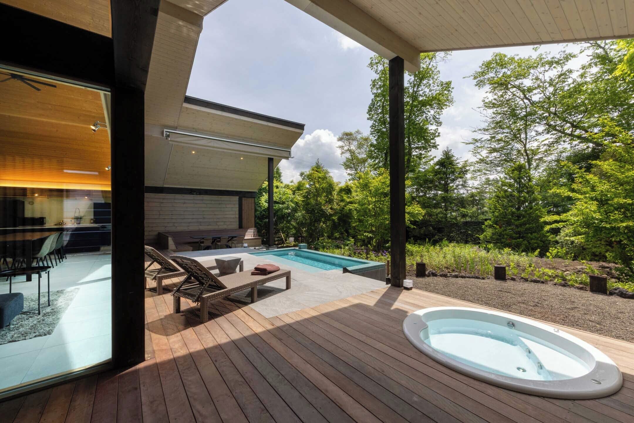 Un área de piscina moderna al aire libre con un jacuzzi, sillones de descanso y una zona de estar cubierta.