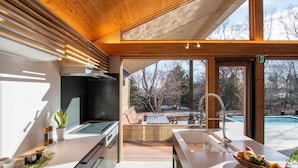 A modern kitchen with a large island, a view of a swimming pool, and a wooden ceiling.