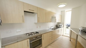 A modern kitchen with stainless steel appliances, wooden cabinets, and a large window providing natural light. - Warwick Conferences - Central Campus Venues  (Coventry)