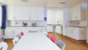 A modern kitchen with white cabinets, a wooden countertop, and a dining area with a white table and colorful chairs. - Warwick Conferences - Central Campus Venues  (Coventry)