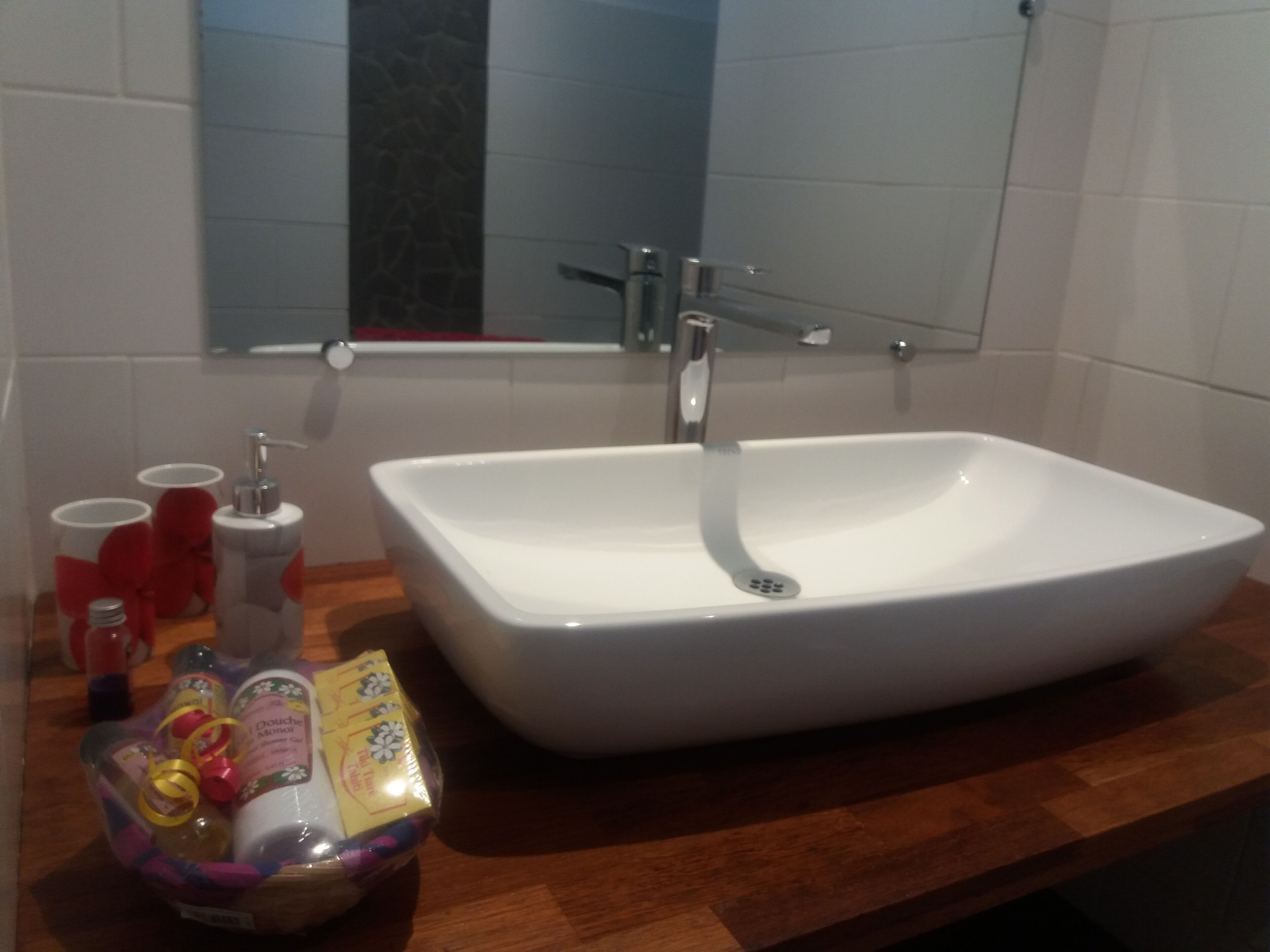 Et badeværelse med en hvid vask, et spejl og et badekar. Der er toiletartikler på bordet.