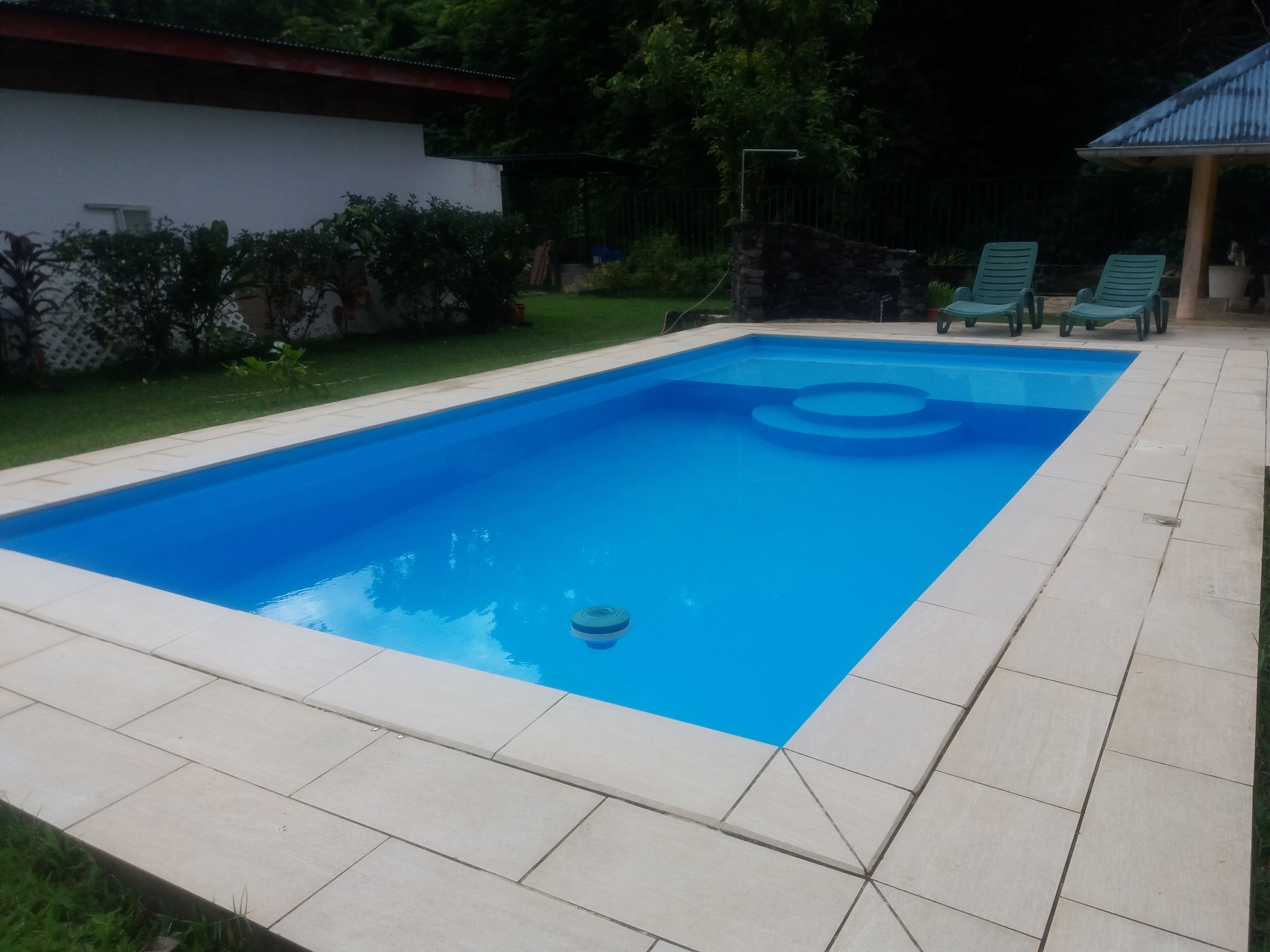 A rectangular swimming pool with a blue interior, surrounded by a tiled deck.