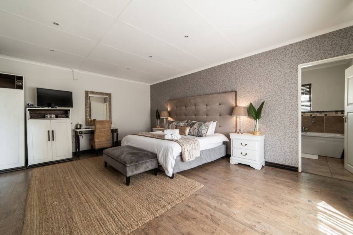 Ein modernes Schlafzimmer mit einem großen Bett, Nachttischen, einem Fernseher und einem durch eine geöffnete Tür einsehbaren Badezimmer.
