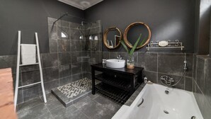 Une salle de bain moderne avec une douche à parois de verre, un lavabo blanc, un meuble-lavabo noir et une grande baignoire.