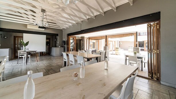 Une pièce spacieuse avec une grande table en bois, des chaises blanches et un tableau blanc. Le plafond est doté de poutres apparentes et un lustre y est suspendu.