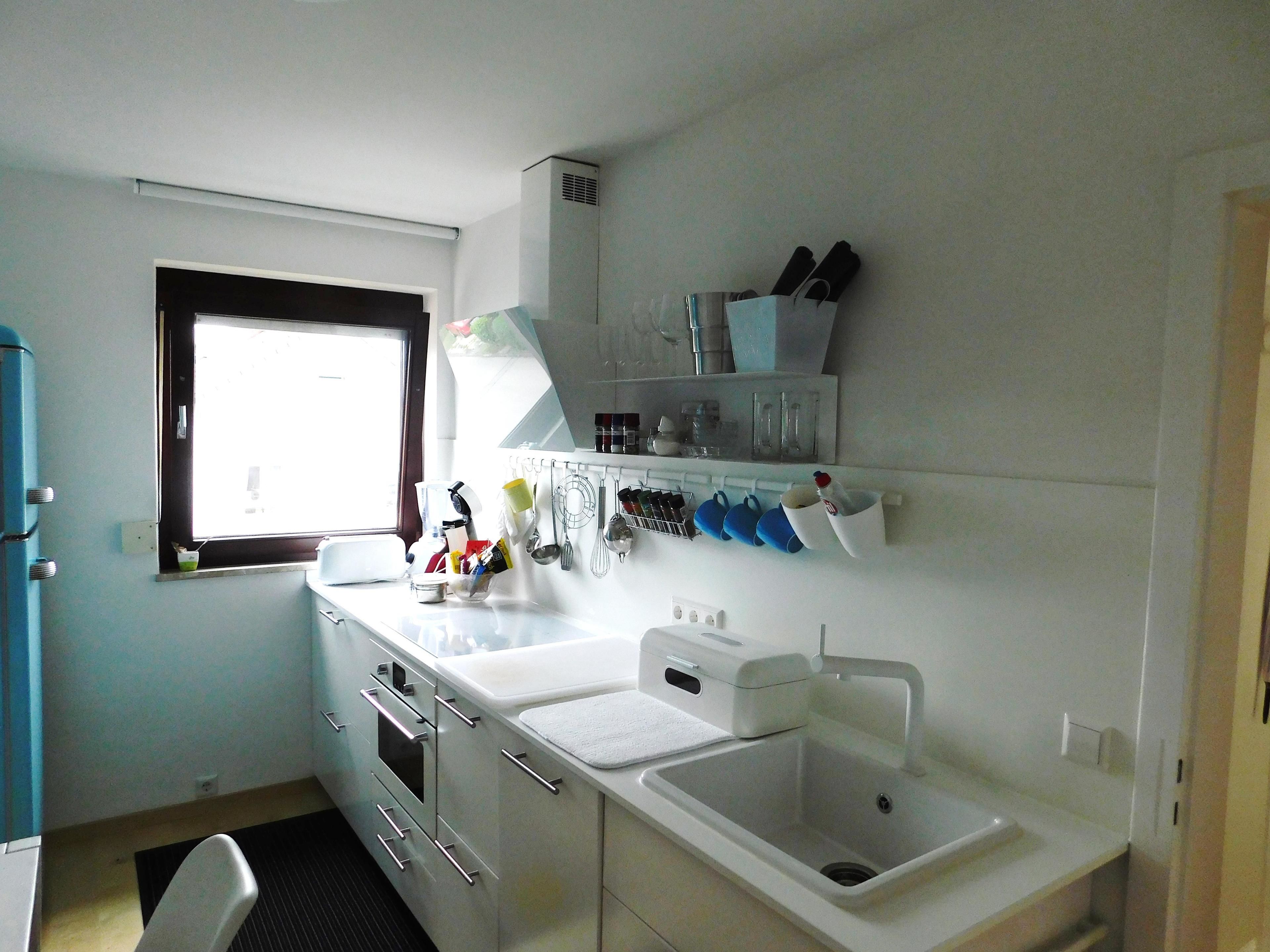 A compact kitchen with white appliances, a window, and a countertop with various utensils and containers.