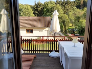 A balcony with a wooden floor, a white table with a lamp, and two white umbrellas.