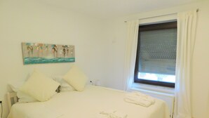 A neatly made bed with white linens, a painting on the wall, and a window with blinds. - Ferienapartments Ida (Lorch)