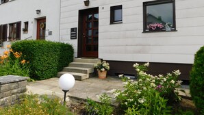A white building with a brown door and windows, a small porch with steps, and a street lamp. - Ferienapartments Ida (Lorch)