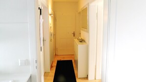 A narrow hallway with a black rug, a white door at the end, and a small white cabinet with a mirror above it. - Ferienapartments Ida (Lorch)