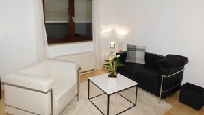 A modern living room with a white sofa, a black sofa, a white coffee table, and a window with curtains. - Ferienapartments Ida (Lorch)