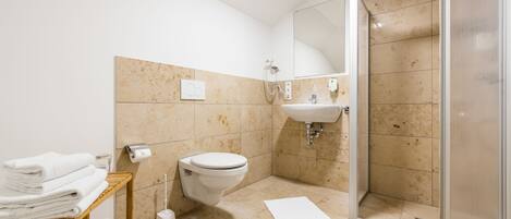 Un baño con inodoro, lavabo, ducha y un estante de madera con toallas.