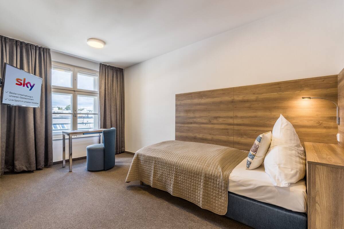 Habitación de hotel con cama, escritorio y televisión mostrando el logotipo de Sky.