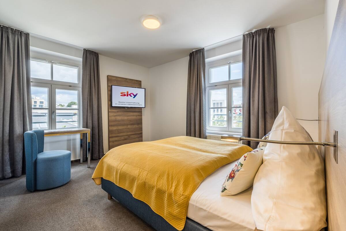 Habitación de hotel con cama, escritorio, silla y televisor mostrando el logotipo de SKY.