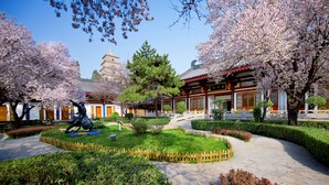 A traditional Japanese garden with a statue, a pagoda, and a building with a red roof.