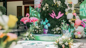 A stage with a backdrop of tropical plants and balloons, a bench, and a floral arrangement.