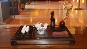A wooden tray with tea utensils, a teapot, a vase with flowers, and a folded towel on a polished floor.