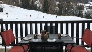 A table set for two with plates, cups, and a vase, overlooking a snowy ski slope with skiers. - Charming Apartment in Val-Cenis: Ski-In/Ski-Out, Terrace, 4 Guests, Renovated (Lanslevillard)