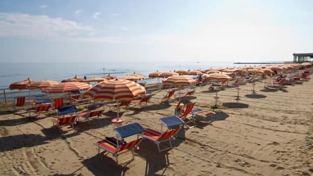 Une plage bordée de rangées de parasols rayés et de chaises de plage.