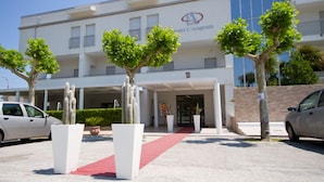 L’entrée d’un hôtel, avec un tapis rouge, des piliers blancs et des arbres.