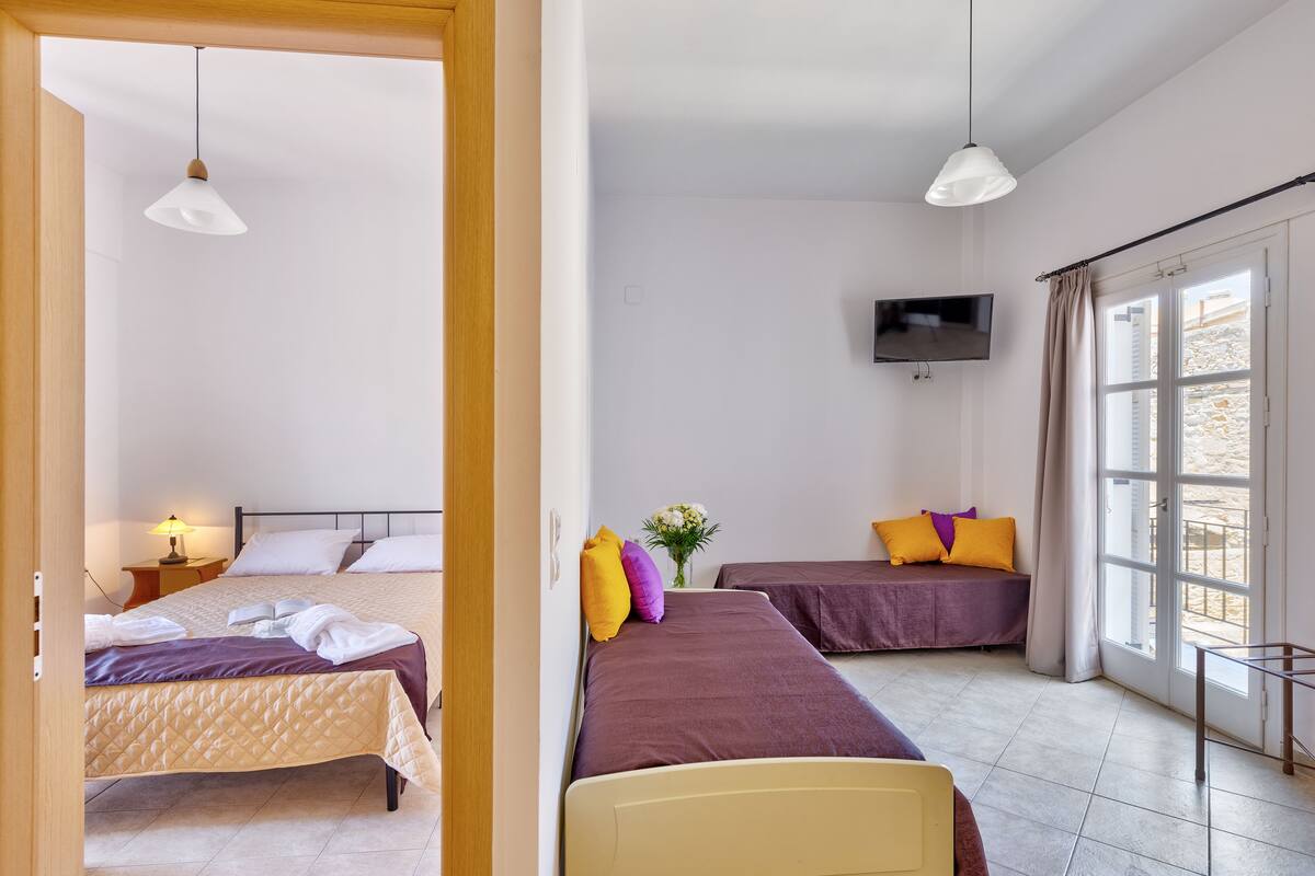 A hotel room with two beds, a TV, a window with curtains, and a bedside table with a lamp.