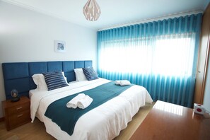 A neatly made bed with a blue headboard, white bedding, and a teal throw blanket. There is a wooden nightstand with a lamp and a framed picture on the wall. - Meriteluna Mountain - Lisbon Sintra and Cascais (Cacém)