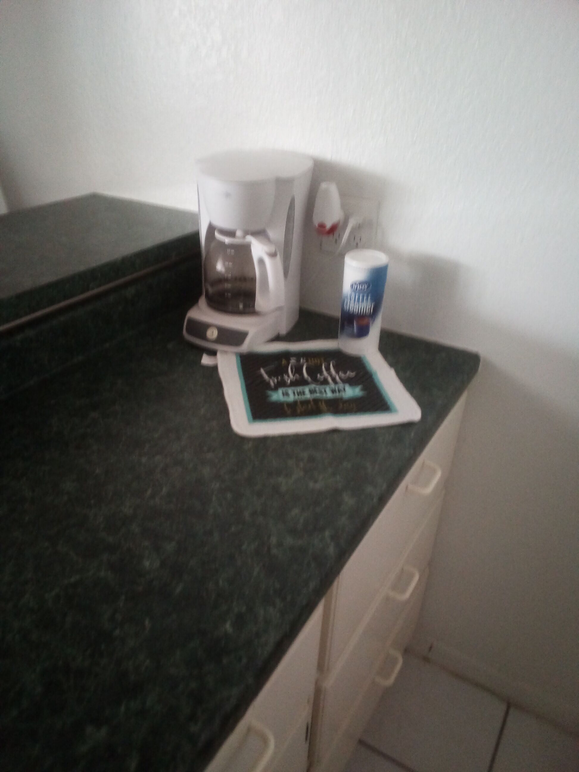 Uma bancada de cozinha com uma cafeteira, uma caneca e um descanso para prato.