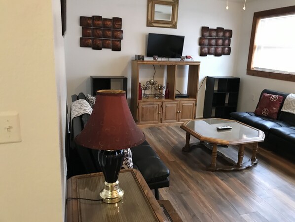 A living room with a wooden coffee table, a red lamp, a black sofa, and a television on a wooden cabinet.