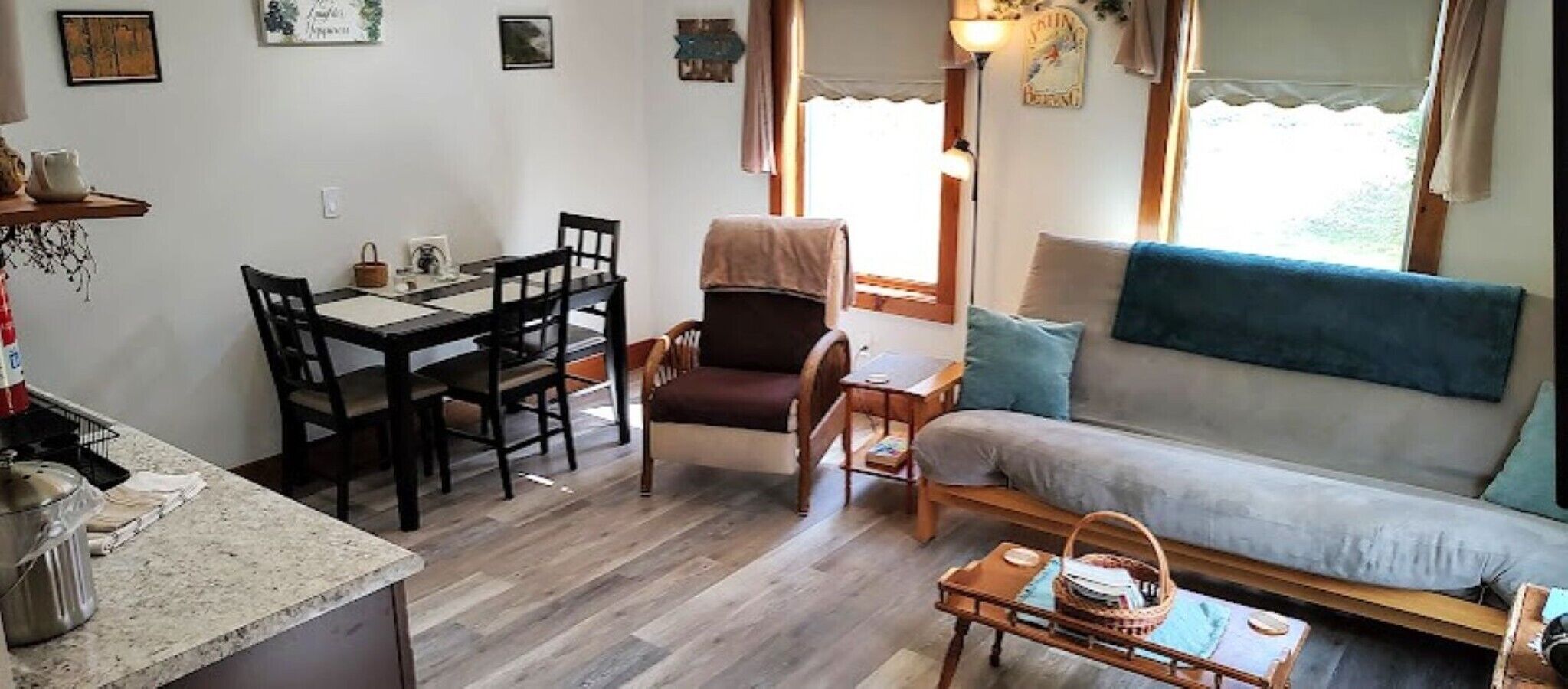 A cozy living room with a sofa, a dining table with chairs, a small table with a basket, and a window with curtains.