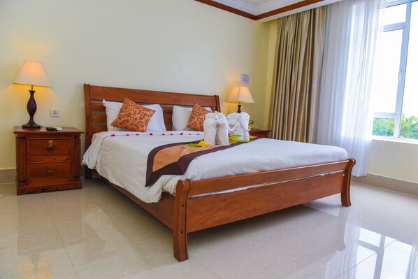 A neatly made bed with a wooden frame, two bedside tables with lamps, and a large window with curtains.