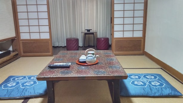 A traditional Japanese room with tatami flooring, a low table with a tea set, and a remote control on the table. - Daishin Ryokan (Choshi)