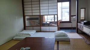 A traditional Japanese-style room with tatami flooring, a low wooden bed, a small table with a chair, and a sliding shoji screen. - Daishin Ryokan (Choshi)