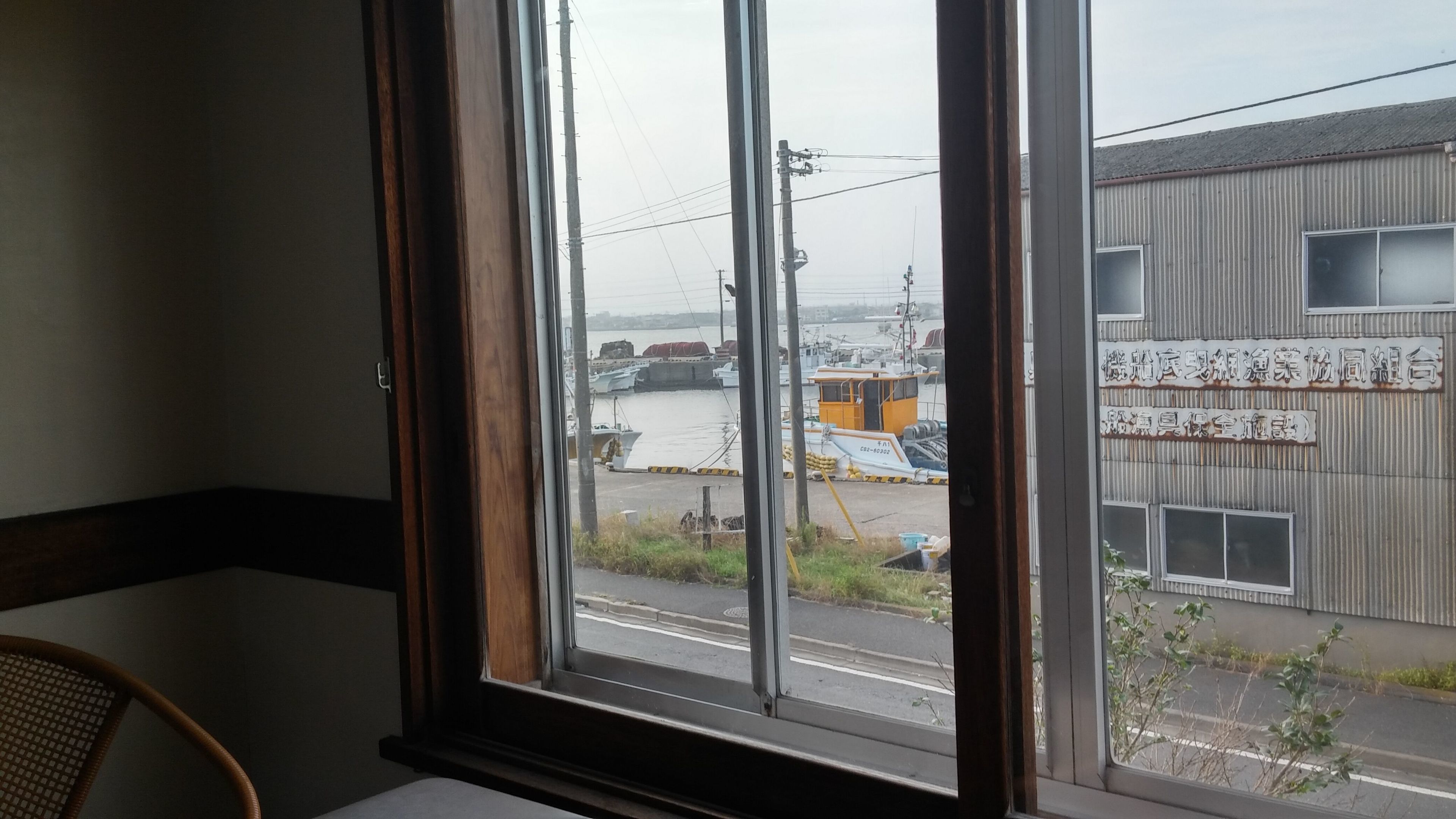 A view from a window with a wooden frame, overlooking a marina with boats and a building with signage.