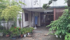 A courtyard with potted plants, a stone pathway, and a building entrance with a sign. - Daishin Ryokan (Choshi)
