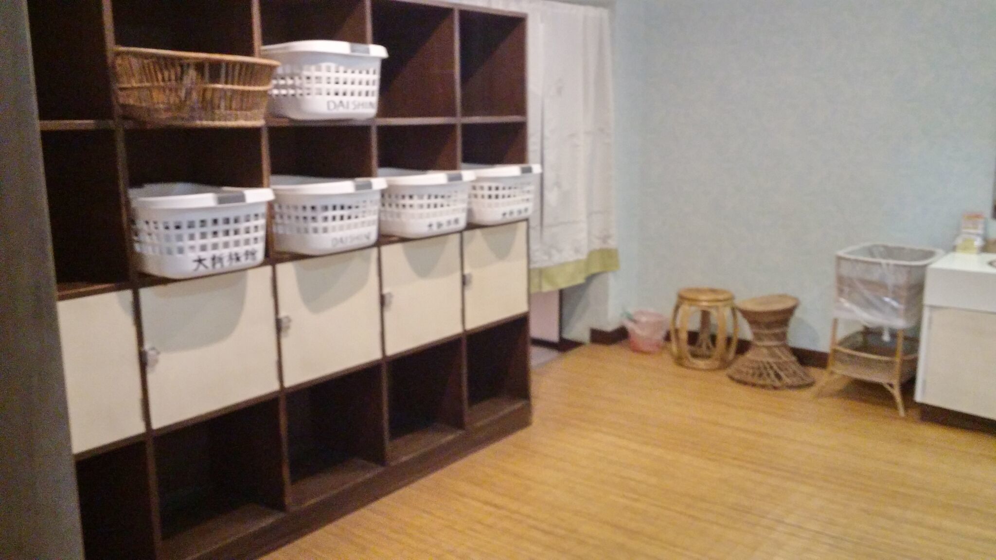 A room with a wooden floor, a white cabinet with multiple compartments, and several white baskets on the shelves.