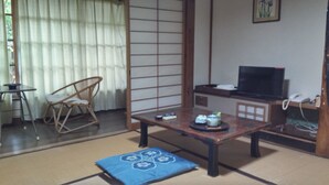 A traditional Japanese-style room with tatami flooring, a low table with a tea set, a television, and a chair. - Daishin Ryokan (Choshi)