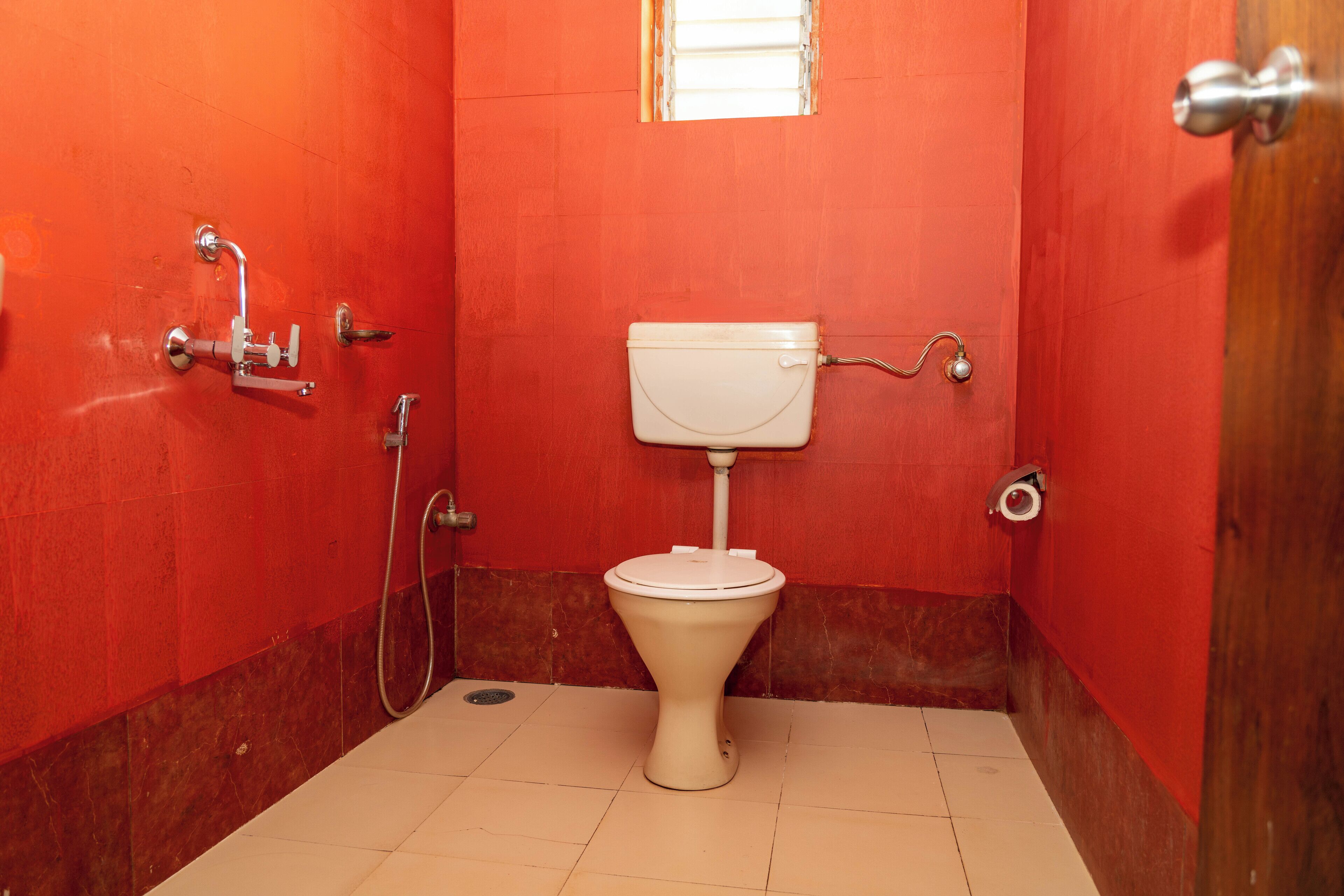 A small, red-walled bathroom with a white toilet, a shower, and a window.