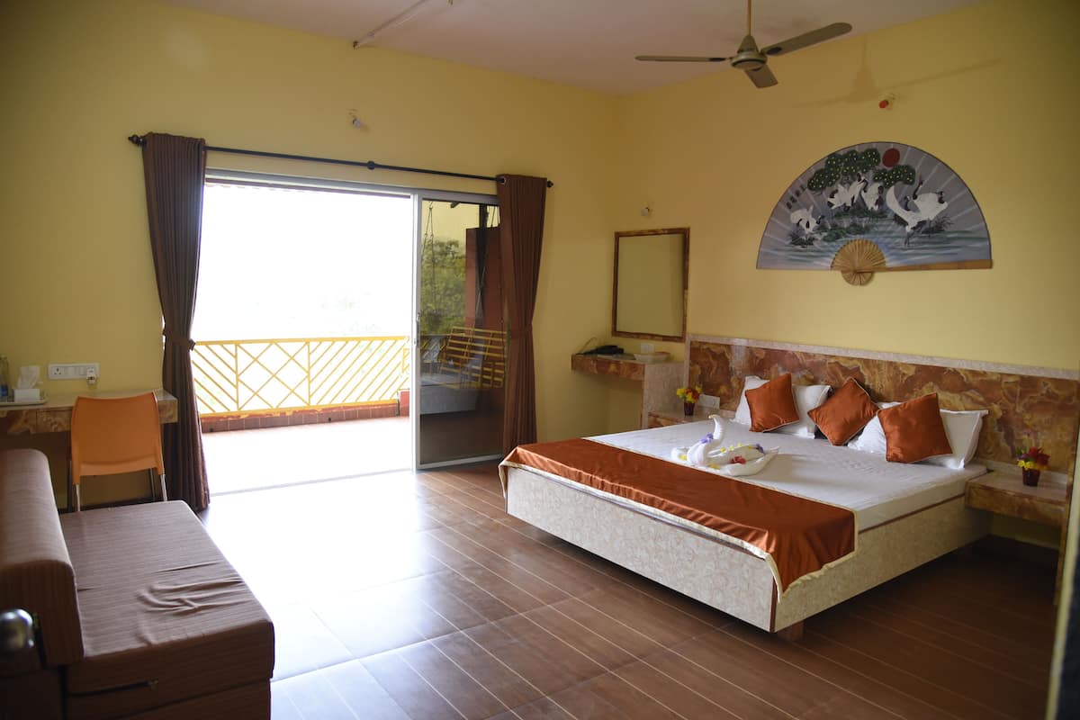 A hotel room with a bed, a desk, a chair, a balcony, and a ceiling fan.